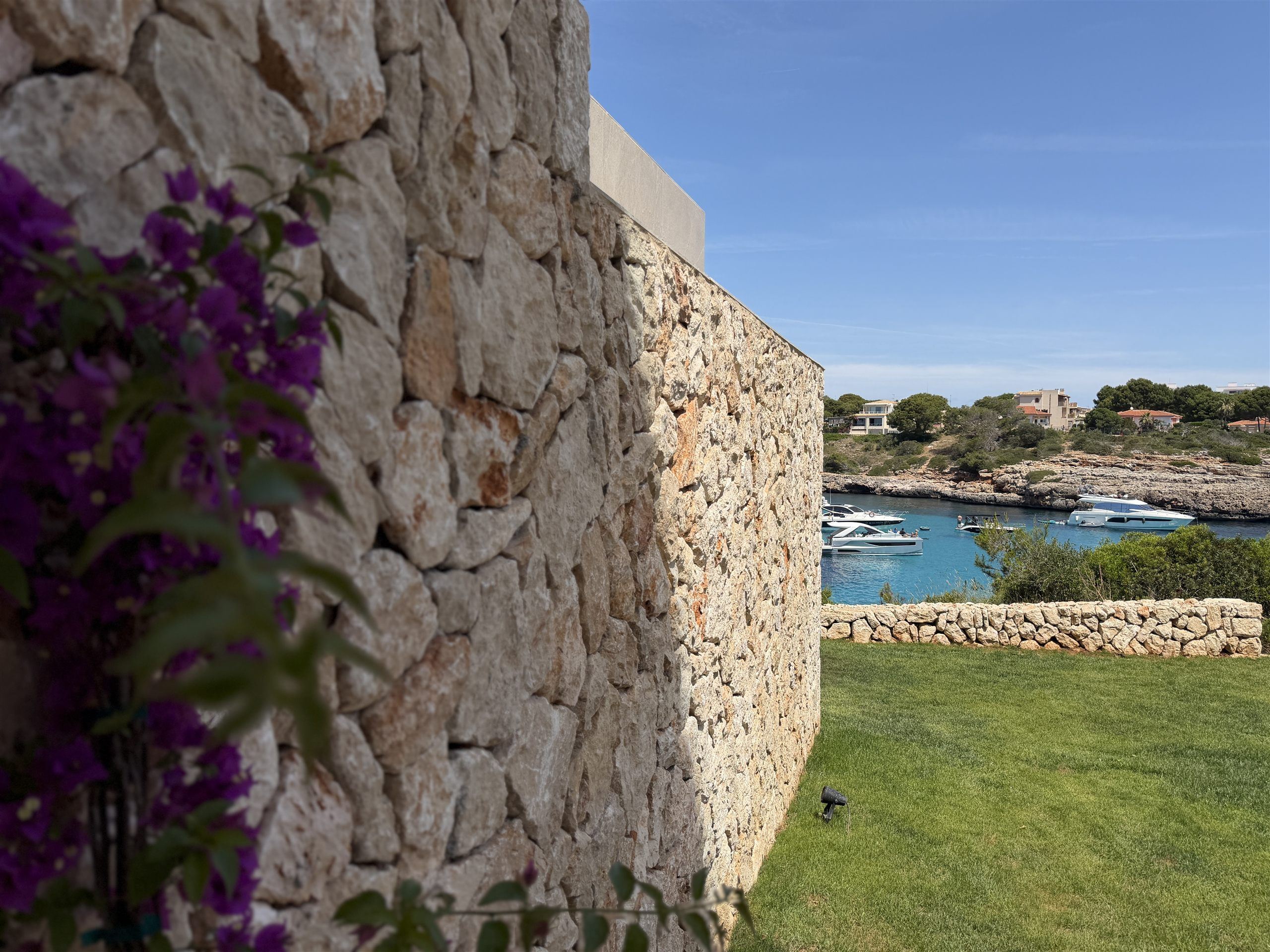 Natursteinmauer mit Bougainvillea und Blick auf die Bucht